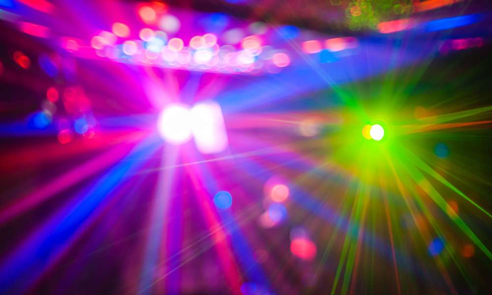 A vibrant display of multicolored lights creates a dynamic, abstract pattern. Bright hues of pink, green, blue, and purple radiate outward, blending together like the energetic scene of a private event or party secured by top-notch security in Oakland County.