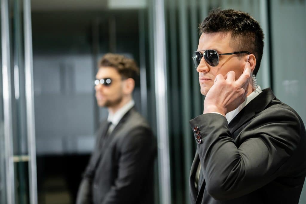 Two security personnel in sunglasses and suits stand vigilant. The one in the foreground speaks into an earpiece, exemplifying the professionalism of Private Security Oakland County, while the other watches keenly from behind, ensuring seamless protection for any special event.